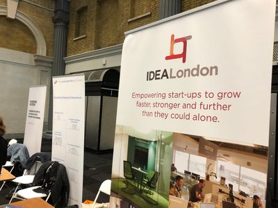 A banner behind a stall advertising Empowering start-ups to grow faster, stronger and further than they could alone. To the left are more stalls with banners of similar corporate speak.