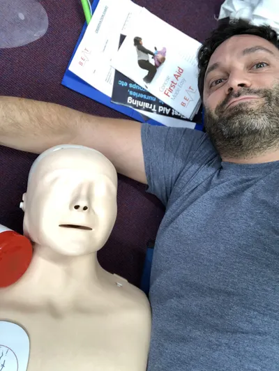 Louie Christie laying next to a first aid mannequin, Louie is smiling.