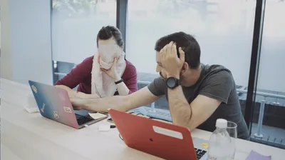 Louie Christie sat at a desk with a woman and he is pointing at a laptop between them. Her face is blurred.