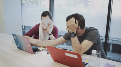 Louie Christie sat at a desk with a woman and he is pointing at a laptop between them. Her face is blurred.